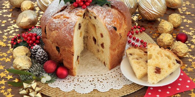 Panettone christams cake and slice with bauble decorations, holly and winter flora over oak background with stars.