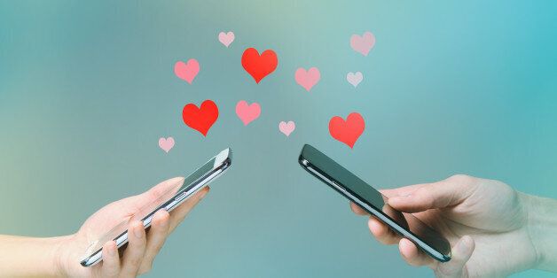 Young man and woman's hands holding smart phones with hearts floating over