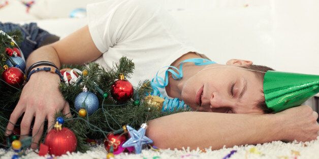 Young drunken man sleeping on floor with Christmas tree and in party hat