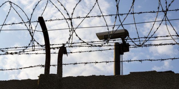 Security camera behind barbed wire fence stretched around prison walls