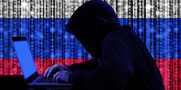 Hacker in a dark hoody sitting in front of a notebook with digital russian flag and binary streams background cybersecurity concept