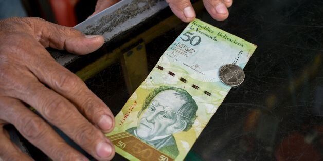 A man compares a new 50-Bolivar-coin with a Bolivar-note of the same denomination at a kiosk in Caracas on December 28, 2016.Venezuela took delivery on December 27 of its third load of new, bigger denomination banknotes, its central bank said, but there was no sign of them in circulation yet despite official promises and mounting public anxiety. Maduro's announcement that the 100-bolivar notes would suddenly no longer be legal tender provoked long lines of people trying to change them, and looting and rioting in some areas, resulting in four deaths. / AFP / FEDERICO PARRA (Photo credit should read FEDERICO PARRA/AFP/Getty Images)