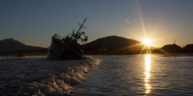 The sun sets near the rusty hulk of a ship that is stranded on the beach in Yuzhno-Kurilsk, the main settlement on the Southern Kuril island of Kunashir September 14, 2015. Russian residents of the island chain at the centre of a dispute between Japan and Russia that has held up a treaty to formally end World War Two hope a diplomatic solution will lure tourists and investment to help refurbish rickety infrastructure. The Southern Kuriles are referred to in Japan as the Northern Territories. Picture taken September 14, 2015. REUTERS/Thomas Peter