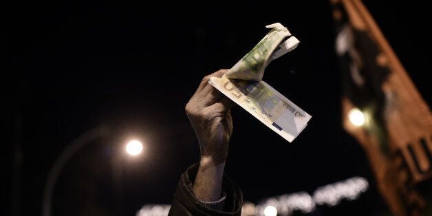 TOPSHOT - A demonstrator holds banknotes during an anti-austerity demonstration of pensioners in central Athens on December 15, 2016. Greek lawmakers on December 15, 2016 approved a pension handout that has set the country on a collision course with hardline European creditors who accuse the struggling eurozone member of defiance / AFP / ARIS MESSINIS (Photo credit should read ARIS MESSINIS/AFP/Getty Images)