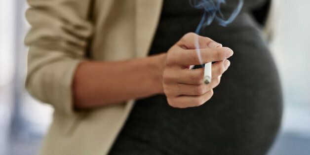 Shot of a woman smoking a cigarette while preganant
