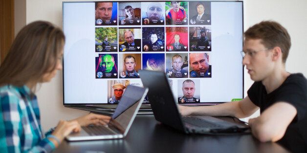 Artem Kuharenko, co-founder of NTechLab, right, works on a laptop computer as the faces of individuals identified by the FindFace facial recognition app sit on a digital screen at the company's offices in Moscow, Russia, on Tuesday, July 12, 2016. FindFace, which has been downloaded for free more than a million times on both Apple and Android platforms since February, allows users to identify strangers at the click of their smartphone cameras as long as long as theyve been previously identified