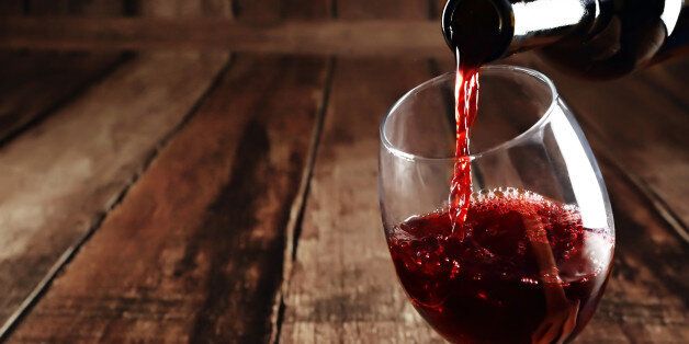 Red wine is poured from bottle to glass, wooden background