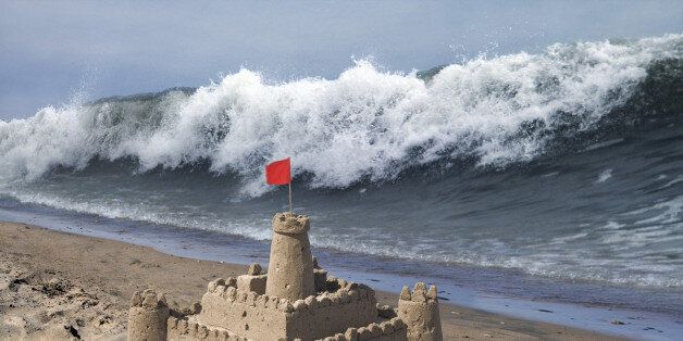 Tidal wave approaching sandcastle with flag
