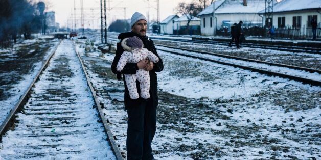 TOPSHOT - A man holds his baby while waiting with other migrants and refugees at a train station for a train in southern Serbian town of Presevo on January 20, 2016. As refugees continued to flow from Greece through the Balkans on their way to western Europe, aid workers sounded alarms over inadequate shelter from the current freezing temperatures and snowy conditions, particularly for children. / AFP / DIMITAR DILKOFF (Photo credit should read DIMITAR DILKOFF/AFP/Getty Images)