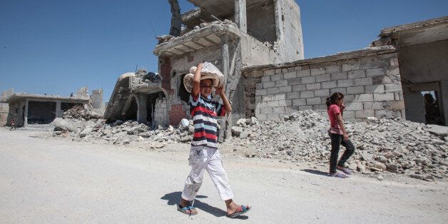 KOBANE, SYRIA - JUNE 20: (TURKEY OUT) A boy carries bread as he walks past the destroyed buildings in the Syrian town of Kobane, also known as Ain al-Arab, Syria. June 20, 2015. Kurdish fighters with the YPG took full control of Kobane and strategic city of Tal Abyad, dealing a major blow to the Islamic State group's ability to wage war in Syria. Mopping up operations have started to make the town safe for the return of residents from Turkey, after more than a year of Islamic State militants holding control of the town. (Photo by Ahmet Sik/Getty Images)