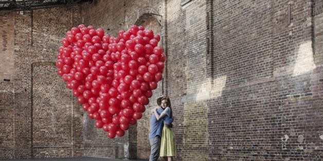 Couple hugging in empty warehouse with red heart made of balloons