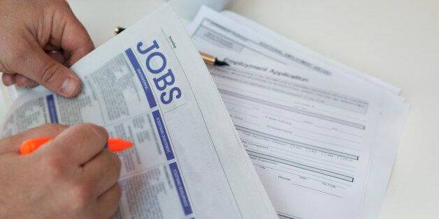 Close-up of hands finding jobs in newspaper with cup in background.