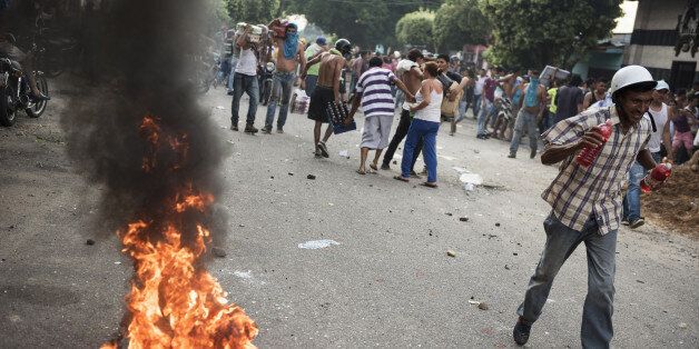 People walk past a tire set on fire by demonstrators during a protest in La Fria, Tachira, Venezuela, on Saturday, Dec. 17, 2016. The largest denomination of Venezuela's crippled currency was pulled from circulation before the new, larger-denomination bills were able to enter it, ATMs and wallets are mostly empty, and Christmas is just a little more than a week away. Photographer: Carlos Becerra/Bloomberg via Getty Images