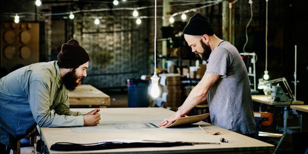 Two leatherworkers discussing product design at table in leather workshop