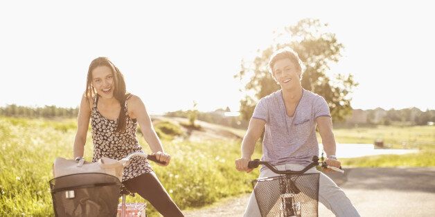 Portrait of happy young couple with legs apart cycling on country road