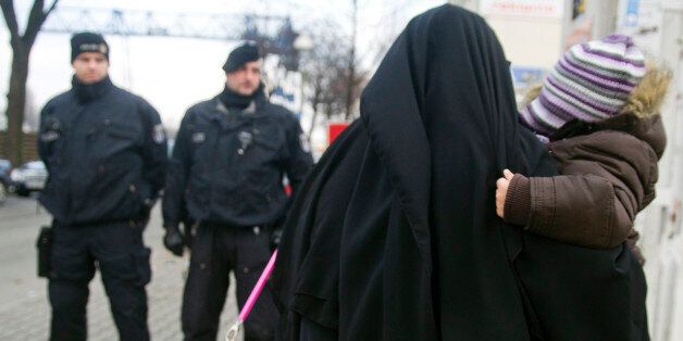 BERLIN, GERMANY - JANUARY 13: A Muslim woman, wearing a burqa, carries a child as she walks past police outside a building where Salafites are holding a benefit rally for Syrian Muslims on January 13, 2013 in Berlin. Two dozen members of 'Pro Deutschland' waited in the centre of Berlin for Salafites who originally planned to hold a public gathering to raise money for Muslims in Syria, which included prominent speakers such as radical Islamic preacher Pierre Vogel. They then moved the event to a private gathering in Neukoelln district. Salafites are an ultra-conservative group of Muslim sunnis with hundreds of members in Berlin and the area around Bonn and cologne. German authorities are keeping a close eye on the group, espacially since clashes that broke out last year in which Salafite demonstrators attacked police and right-wing counter-demonstrators. on January 13, 2013 in Berlin, Germany. (Photo by Target Presse Agentur Gmbh/Getty Images)