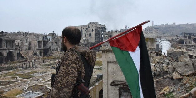 A member of the Syrian pro-government forces walks holding a Palestinian flag in the old city of Aleppo on December 13, 2016 after they captured the area. After weeks of heavy fighting, regime forces were poised to take full control of Aleppo, dealing the biggest blow to Syria's rebellion in more than five years of civil war. / AFP / George OURFALIAN (Photo credit should read GEORGE OURFALIAN/AFP/Getty Images)