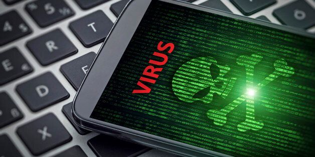 Virus alert on the screen of smartphone on laptop computer. Skull of death on data flowing background. Selective focus on screen of the phone.