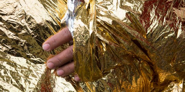 Close-up of an Afghan refugee's hand sticking out from a foil blanket in the port of Mytilene on the Greek island of Lesbos