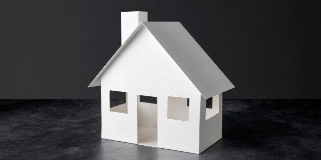 Three dimensional model house constructed from white paper set against a dark background.