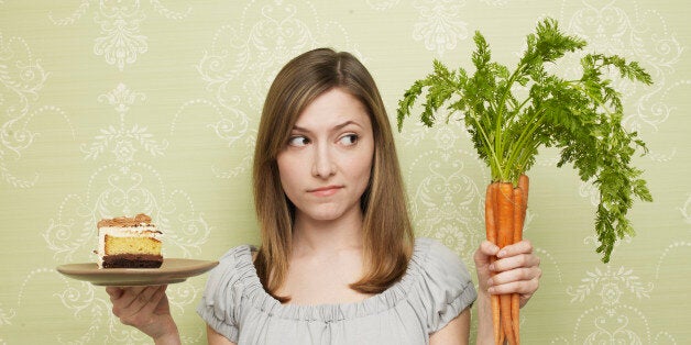 Young woman choosing cake or carrots, indoors