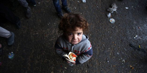 TOPSHOT - A Syrian child, who fled with his family from rebel-held areas in the city of Aleppo, reacts as he holds a sandwich on December 1, 2016, at a shelter in the neighbourhood of Jibrin, east of Aleppo. / AFP / Youssef Karwashan (Photo credit should read YOUSSEF KARWASHAN/AFP/Getty Images)