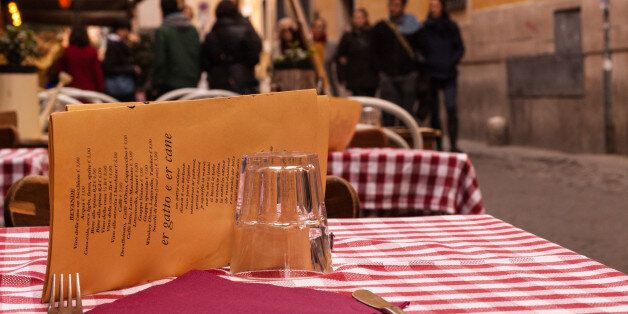 Close-up on a table of an outdoor Italian restaurant with medieval alley and people walking in the background