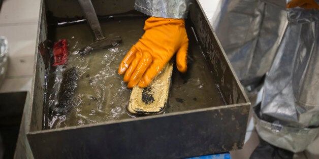 A worker cleans just melted gold alloy bar in a workshop of Altyntau gold mine extraction factory outside northern Kazakhstan's town of Kokshetau June 13, 2013. The gold industry has released new guidelines for bullion miners under pressure to disclose the real economics of producing an ounce of metal, feeding a debate over the sustainability of many gold mines in a sector battered by falling prices. Picture taken June 13, 2013. REUTERS/Shamil Zhumatov (KAZAKHSTAN - Tags: BUSINESS COMMODITIES)