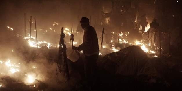 People try to extinguish fires with buckets at the moria migrants camp on the island of Lesbos early on November 25, 2016. Angry migrants set fire to a camp on the Greek island of Lesbos after a woman and a six-year-old child died following a gas cylinder explosion, local police said. / AFP / STR (Photo credit should read STR/AFP/Getty Images)