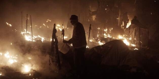 People try to extinguish fires with buckets at the moria migrants camp on the island of Lesbos early on November 25, 2016. Angry migrants set fire to a camp on the Greek island of Lesbos after a woman and a six-year-old child died following a gas cylinder explosion, local police said. / AFP / STR (Photo credit should read STR/AFP/Getty Images)