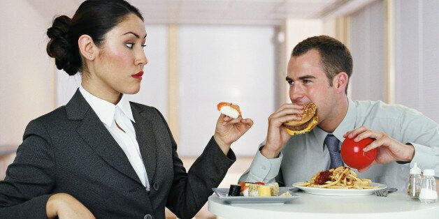 Two colleagues having lunch, man eating burger, woman holding sushi