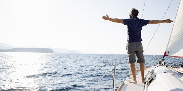 man stands at bow of yacht with arms outstretched