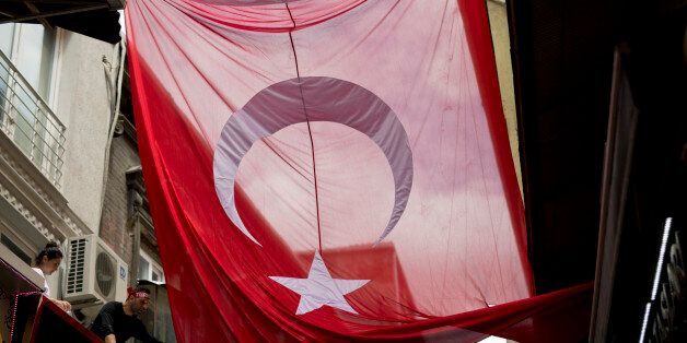 A man tries to unwrap a giant Turkish flag at Grand bazaar, one of the largest and oldest covered markets in the world, in Istanbul, Monday, July 18, 2016. The European Union and the United States expressed alarm Monday with Turkey's response to a failed coup, telling the NATO member and EU aspirant that it must uphold democracy and human rights as it pursues the military officers and anyone else involved in the plot. (AP Photo/Petros Giannakouris)