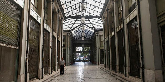 A pedestrian walks past closed and shuttered shops inside a shopping arcade in Athens, Greece, on Sunday, July 12, 2015. European finance chiefs said they were unlikely to strike a deal on the outlines of a third Greek bailout, threatening to delay the cash infusion Prime Minister Alexis Tsipras desperately needs. Photographer: Simon Dawson/Bloomberg via Getty Images