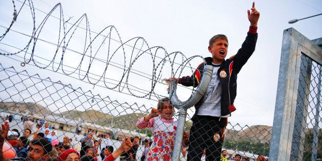 Refugee youths gesture from behind a fence as German Chancellor Angela Merkel, Turkish Prime Minister Ahmet Davutoglu, EU Council President Donald Tusk and European Commission Vice-President Frans Timmermans (all not pictured) arrive at Nizip refugee camp near Gaziantep, Turkey, April 23, 2016. REUTERS/Umit Bektas/File Photo