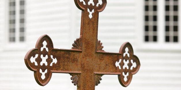 Rusted cemetery cross and white wooden church out of focus. Norway
