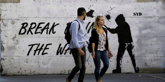 A couple walk in front of a wall with graffiti, near the UN buffer zone,