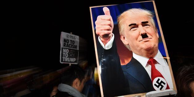 TOPSHOT - A demonstrator holds a placard showing a picture of US President-elect Donald Trump modified to add a swastika and an Adolf Hitler-style moustache during a protest outside the US Embassy in London November 9, 2016 against Trump after he was declared the winner of the US presidential election. Political novice and former reality TV star Donald Trump has defeated Hillary Clinton to take the US presidency, stunning America and the world in an explosive upset fueled by a wave of grassroots anger. / AFP / BEN STANSALL (Photo credit should read BEN STANSALL/AFP/Getty Images)