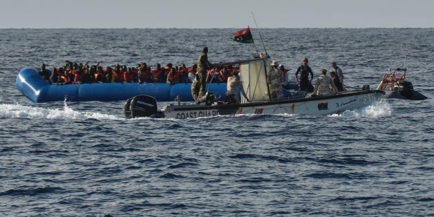 Migrants and refugees sit on a rubber boat as the Libyan coastguards patrol, during a rescue operation of the Topaz Responder, a rescue ship run by Maltese NGO 'Moas' and the Italian Red Cross, on November 4, 2016 off th Libyan coast.Around 750 migrants were rescued across the Mediterranean Thursday by the Italian coast guard, a Frontex ship, a Save The Children vessel, German NGO Jugend Rettet's Iuventa and two boats run by the Malta-based MOAS (Migrant Offshore Aid Station). But at least 110 migrants are feared drowned after they were forced at gunpoint to set sail from Libya, while many more may have died in a separate shipwreck, survivors said. / AFP / ANDREAS SOLARO (Photo credit should read ANDREAS SOLARO/AFP/Getty Images)