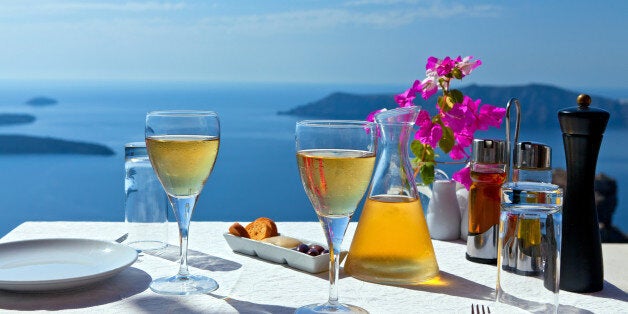 Table and glasses of wine for two people in the restaurant on the beach sea. Greece, Santorini island, view of the Caldera of the volcano.