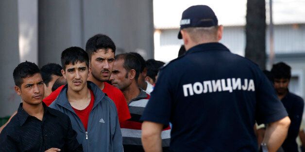 A Serbian police officer stands in front of migrants who wait in line for lunch in the transit center for refugees in Sid, about 100 km west from Belgrade, Serbia, Thursday, Sept. 15, 2016. After the former Balkan migrant route leading from Turkey through Greece, Macedonia, Serbia, Croatia and Slovenia was closed in March, governments are looking for ways to fortify the borders fearing a new massive influx of people from the Middle East, Asia or Africa. Migrants keep on pouring in _ not in tens of thousands, but hundreds a day _ despite an EU-Turkey deal aimed at keeping the migrants away from Europe after more than one million people entered last year. (AP Photo/Darko Vojinovic)