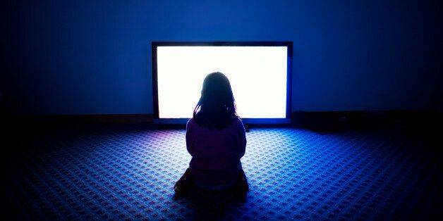 Girl sitting in front of flat screen television in dark room.