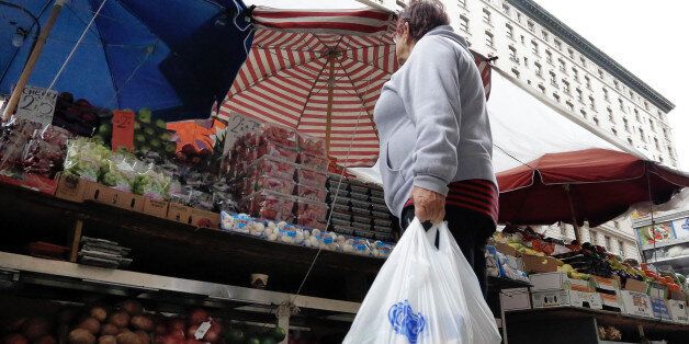 A woman carrying her supermarket purchase in plastic bags stops at a produce vendor on New York's Upper West Side, Thursday, May 5, 2016. Merchants in New York who now hand out billions of free, disposable plastic bags each year to shoppers and diners would have to start charging 5 cents each for the convenient but environmentally unfriendly receptacles under a bill set for a city council vote Thursday. (AP Photo/Richard Drew)