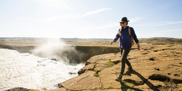 A woman standing on an overlook with a rushing river and waterfall below.