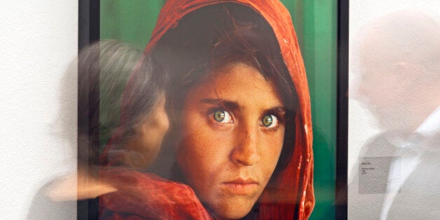 In this picture taken with a long time exposure people walk in front of the photo 'Afghan Girl' (Pakistan, 1984) during the exhibition 'Steve McCurry Retrospective' of US photographer Steve McCurry in the Kunsthalle (Art Hall) in Erfurt, Germany, Wednesday, Feb. 26, 2014. The retrospective shows 120 photographs taken between 1980 and 2012 in countries such as Afghanistan, the United States, Pakistan, India, Tibet, Kashmir, Cambodia, Indonesia, Burma and Kuwait. The exhibition lasts until April 22, 2014. (AP Photo/Jens Meyer)