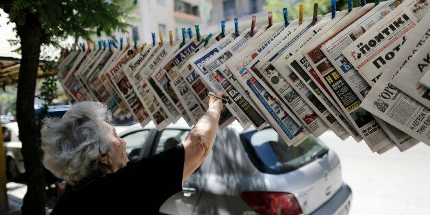 A woman reaches for a newspaper at a news kiosk in Thessaloniki, Greece, on Sunday, July 12, 2015. European finance aides worked through the night struggling to overcome a deadlock over how to keep Greece in the euro after an impasse among their bosses forced a second day of emergency talks. Photographer: Konstantinos Tsakalidis/Bloomberg via Getty Images