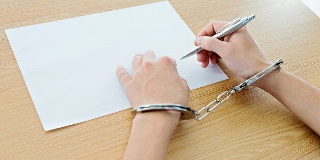 Close up of man hands in handcuffs writing on paper.