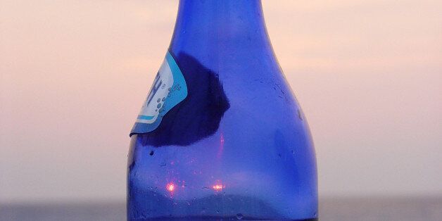 A half full blue bottle of water in front of a red sunset on the island of Lefkada, in Greece.