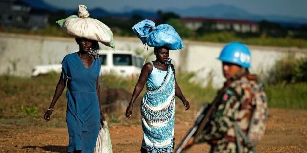 Displaced women carry goods as a Nepalese peacekeeper from the United Nations Mission in South Sudan (UNMISS) patrols outside the premises of the UN Protection of Civilians (PoC) site in Juba on October 4, 2016. According to the UN, due to the increase of sexual violence outside the PoC, UNMISS has intensified its patrols in and around the protection sites, as well as in the wider Juba city area, sometimes arranging special escorts for women and young girls. / AFP / ALBERT GONZALEZ FARRAN (Photo credit should read ALBERT GONZALEZ FARRAN/AFP/Getty Images)