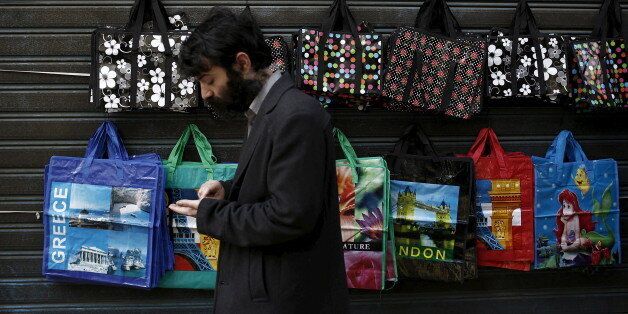 A pedestrian counts money as he walks past shopping bags hanging for sale by a street vendor in Athens, April 22, 2015. Greece will continue to reject creditors' demands for pension cuts and a hike in the value-added-tax (VAT) on islands frequented by tourists, State Minister Nikos Pappas said on Wednesday, in a setback for hopes that a deal could be struck soon. REUTERS/Kostas Tsironis